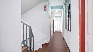 Un couloir avec un escalier en bois, un panneau indiquant la sortie de secours et une fenêtre avec des barreaux en métal.