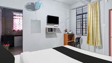 Une chambre d’hôtel avec un lit, une télévision, un bureau, une chaise et une fenêtre avec des rideaux.