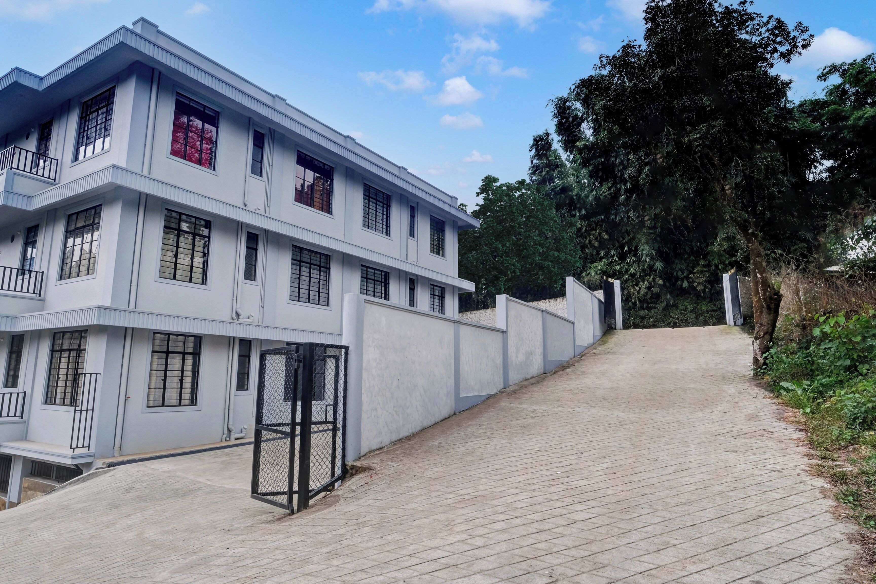 A multi-story building with a flat roof, a gated entrance, and a paved pathway leading up to it.