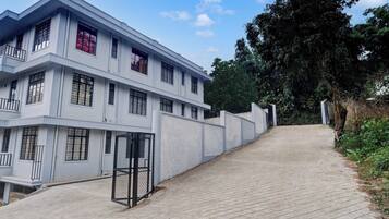 A multi-story building with a flat roof, a gated entrance, and a paved pathway leading up to it.