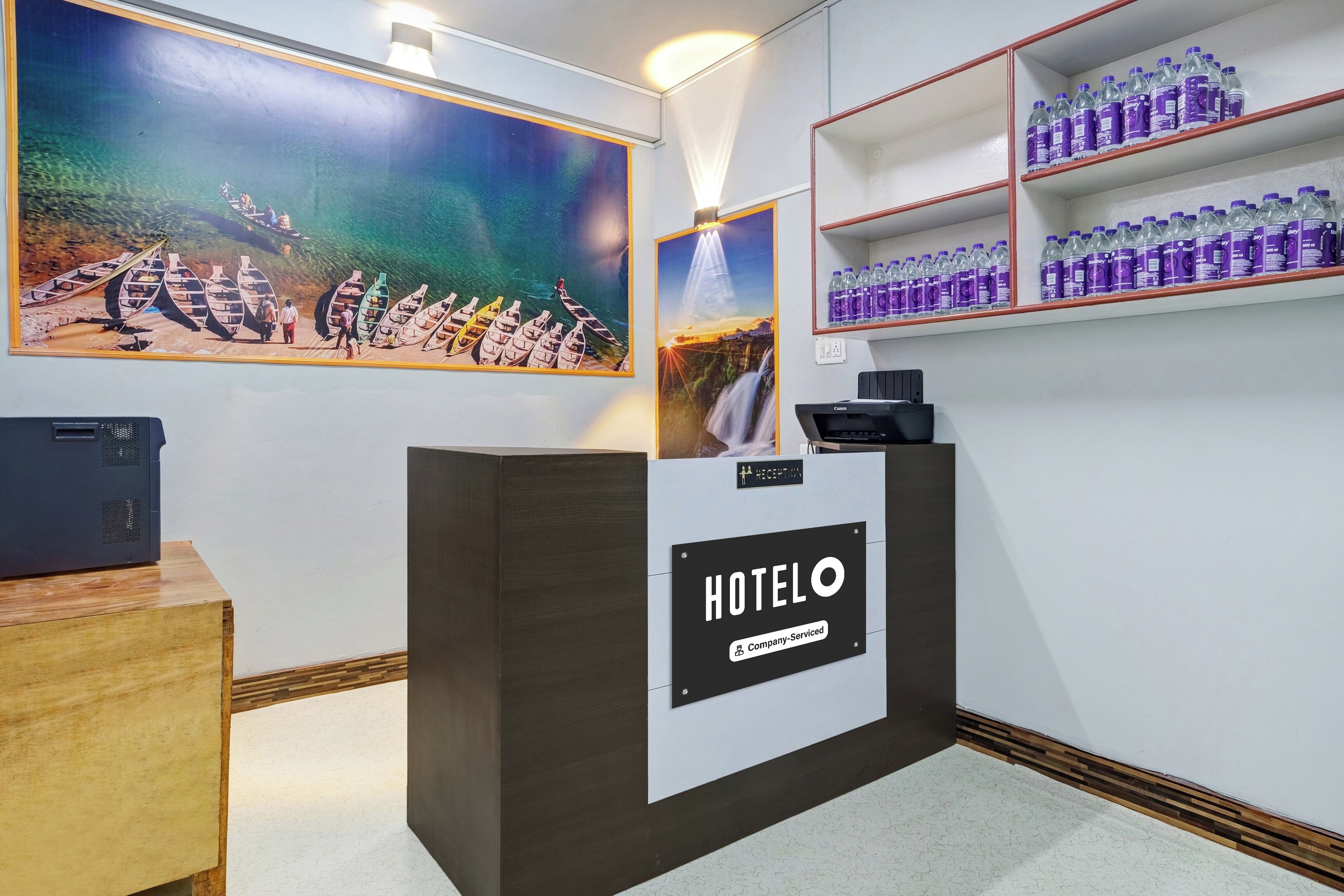 Un comptoir d’accueil avec une enseigne « HÔTEL », une imprimante Canon et un distributeur d’eau placés sur des étagères.