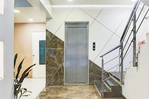 Un ascensor moderno con pantalla digital, pared de mármol y escalera con barandilla de metal.