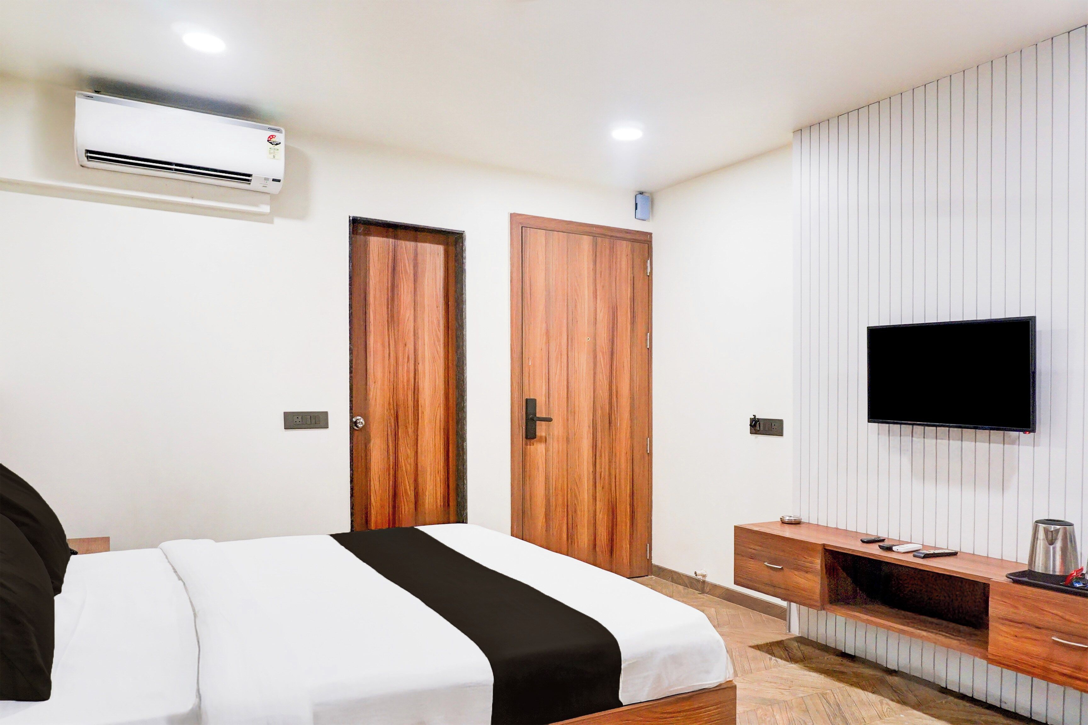 A hotel room with a bed, a TV, a wardrobe, and a small desk with a kettle.