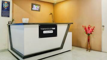 A reception desk with a sign indicating it is company-serviced. There is a ceiling fan above and a framed picture on the wall.