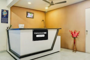 Un mostrador de recepción con un cartel que indica servicio de la empresa. Hay un ventilador de techo arriba y un cuadro enmarcado en la pared.