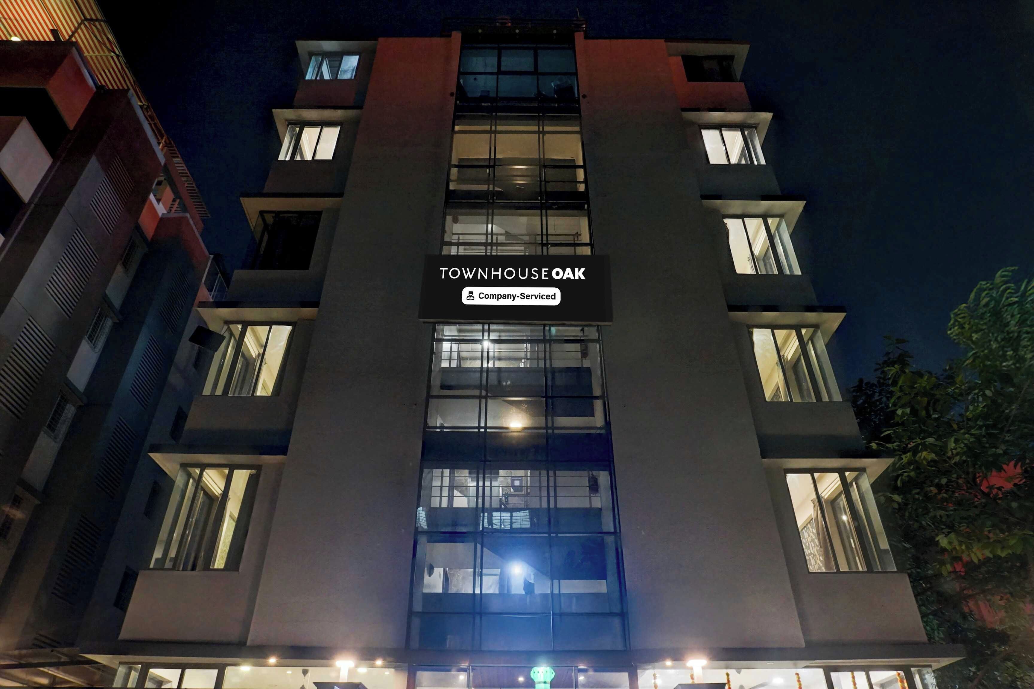 Un immeuble à plusieurs étages, sur lequel on peut lire l’inscription « TOWNHOUSE OAK » et la mention « Services d’entreprise », indiquant qu’il s’agit d’un complexe d’appartements avec services.