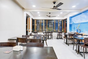 Un comedor con mesas y sillas, ventiladores de techo y un mural en la pared.