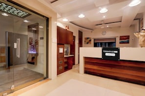 Zona de recepción con entrada por puerta de cristal, mostrador de madera y un reloj en la pared.