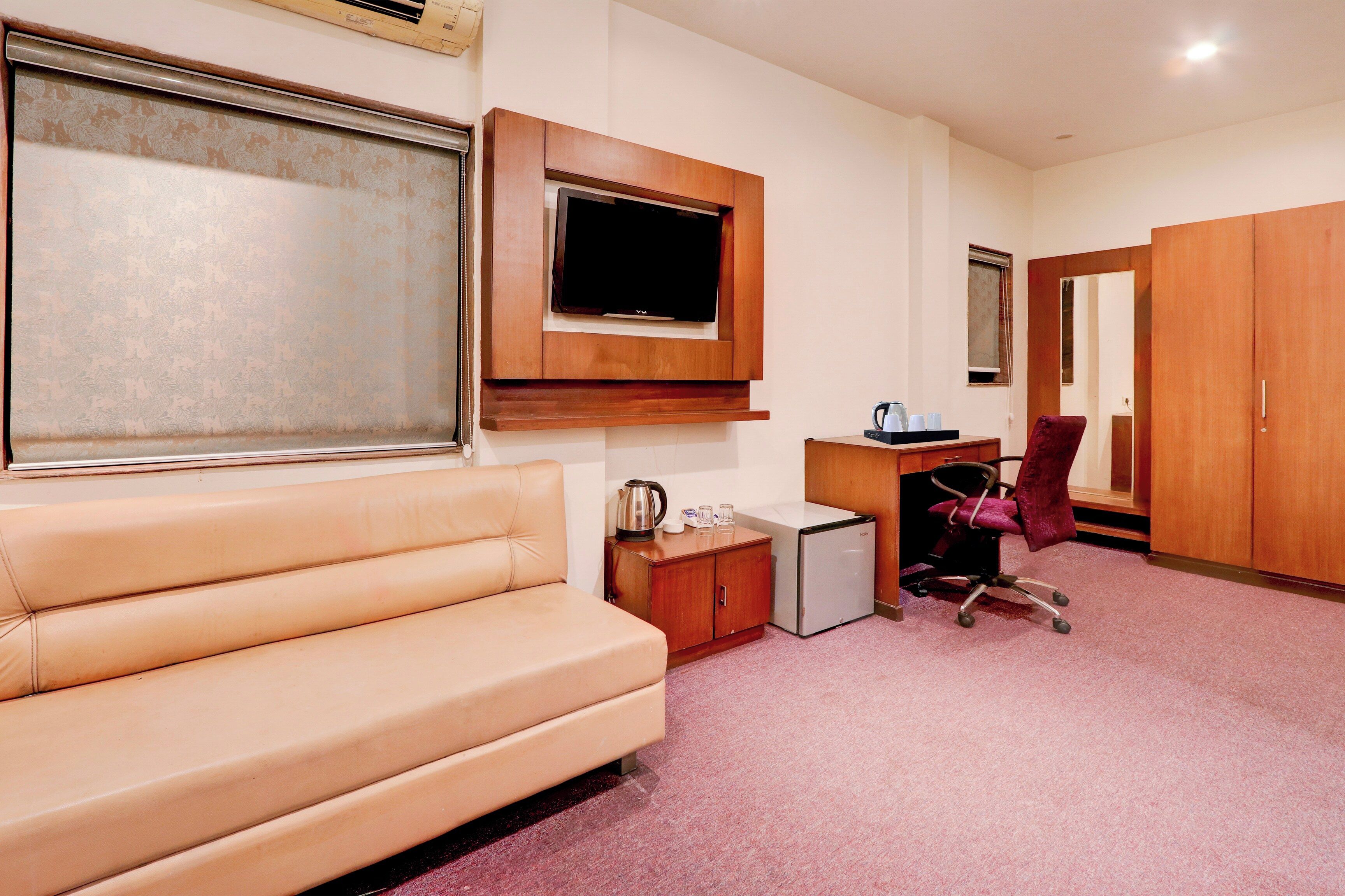 A hotel room with a sofa, a small desk with a kettle, a television, and a wardrobe.