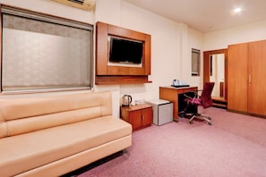 Habitación de hotel con sofá, escritorio pequeño con hervidor, televisión y armario.