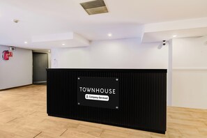 Tauleller de recepció amb un rètol que diu 'TOWNHOUSE Company-Serviced' en un interior modern amb terres de fusta i parets blanques.