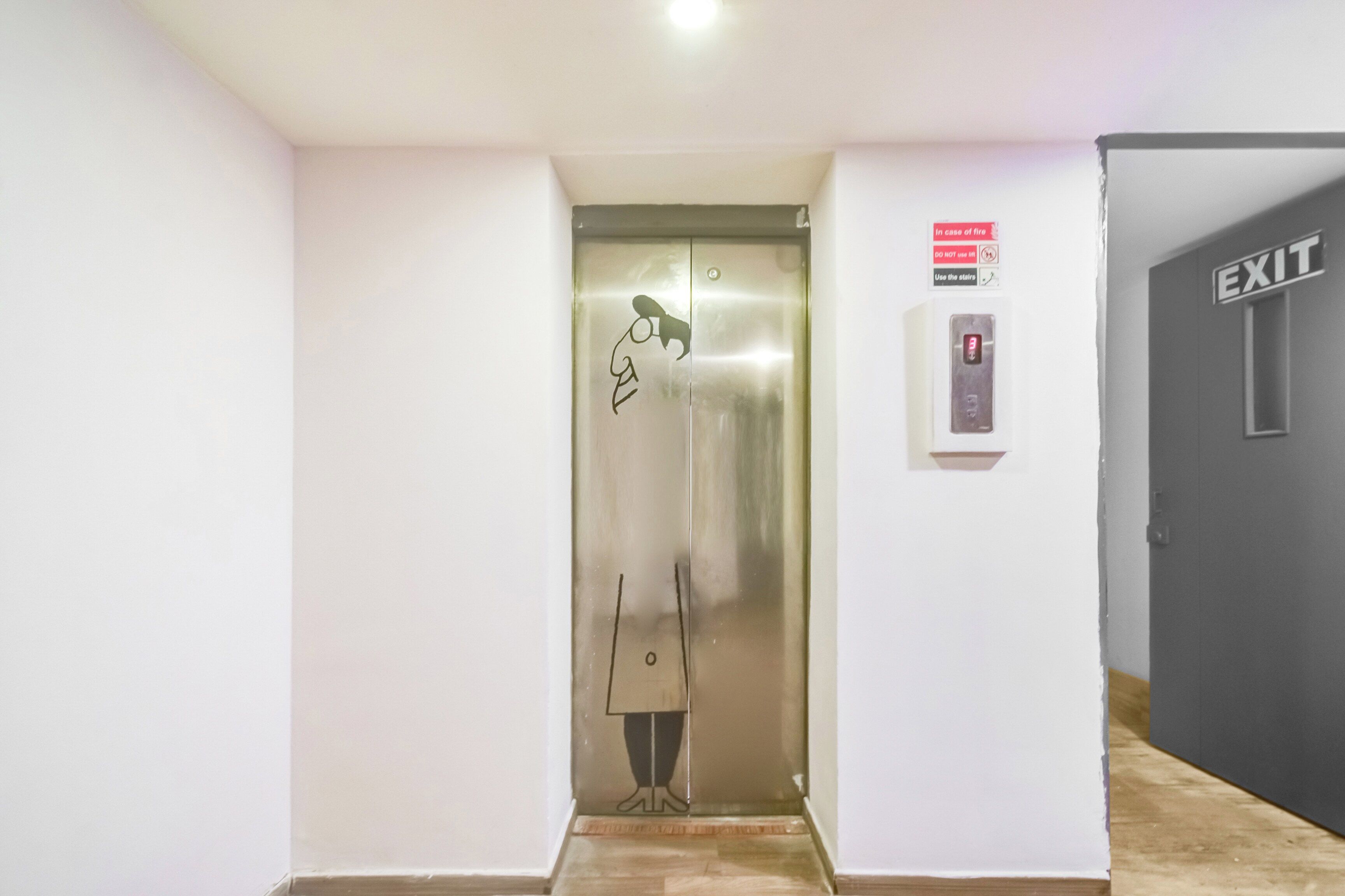 Un ascensor con pantalla digital, un letrero de seguridad contra incendios y una señal de salida.
