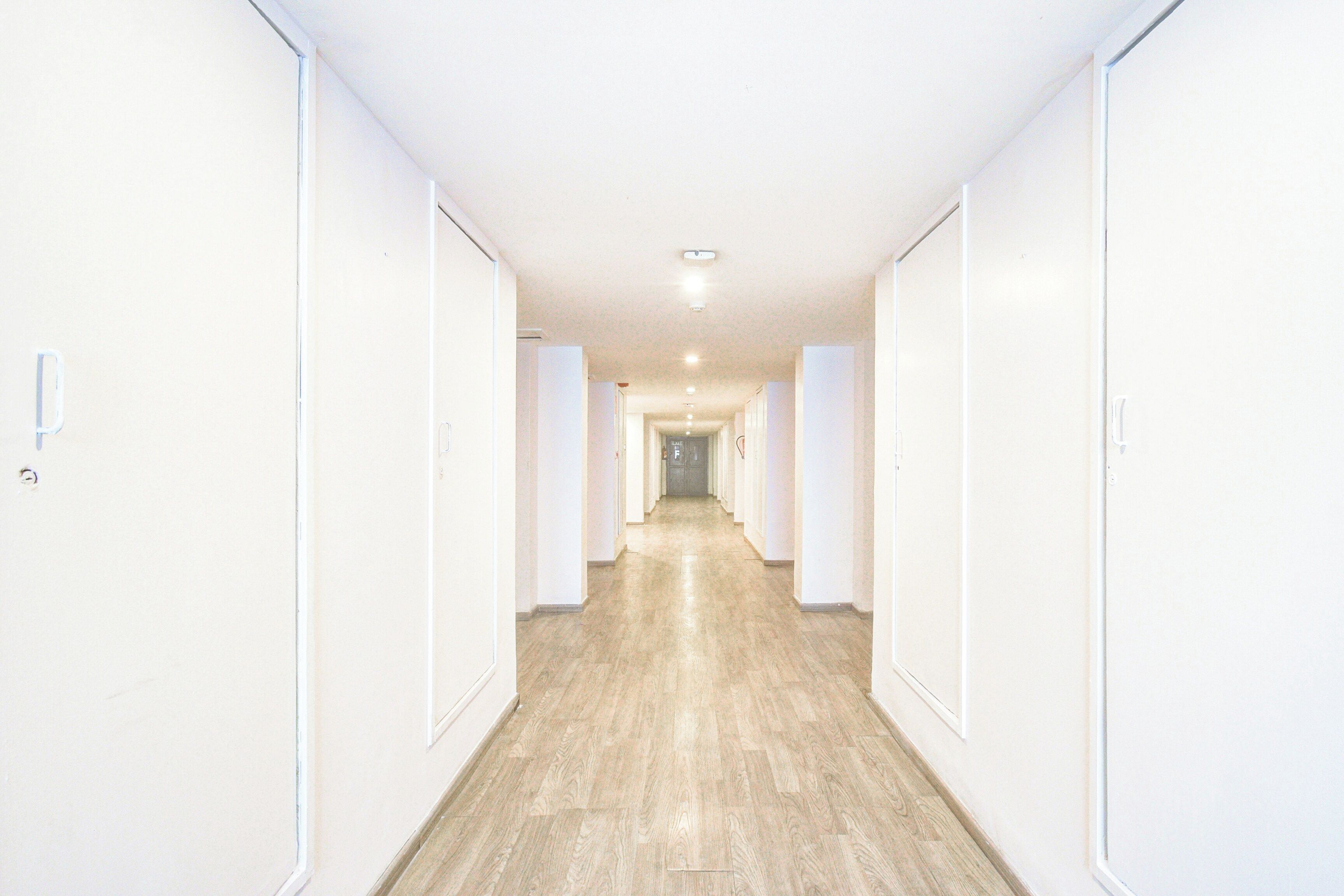 Un pasillo con paredes blancas y puertas que conduce a una habitación con piso de madera.