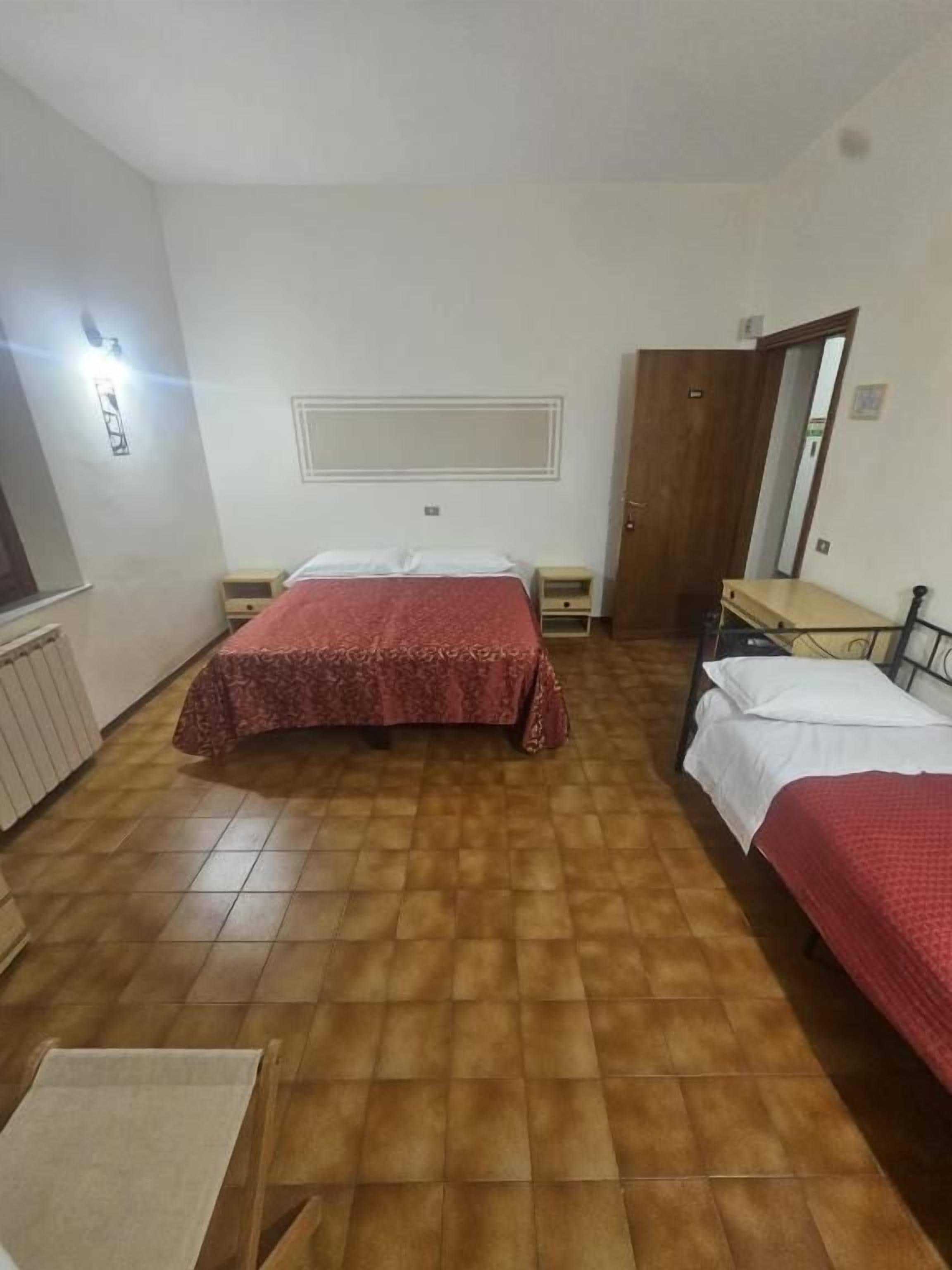 Hotellihuone, jossa on kaksi sänkyä, puulattia, pieni pöytä ja peili.