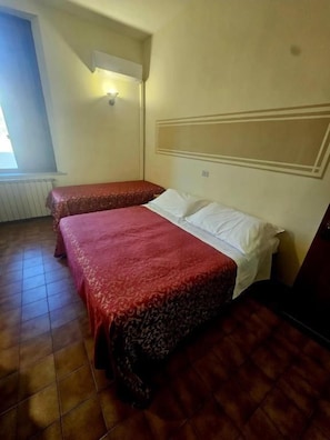 Una habitación con dos camas, un radiador, una lámpara de pared y una ventana.