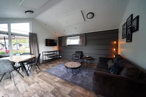 A modern living room with a dining area, a sofa, a TV, and a large window. - Chalet near Efteling Theme Park (Kaatsheuvel)