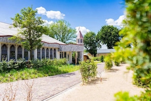 A stone building with arched windows and a tower, surrounded by greenery and a paved path. - Chalet near Efteling Theme Park (Kaatsheuvel)
