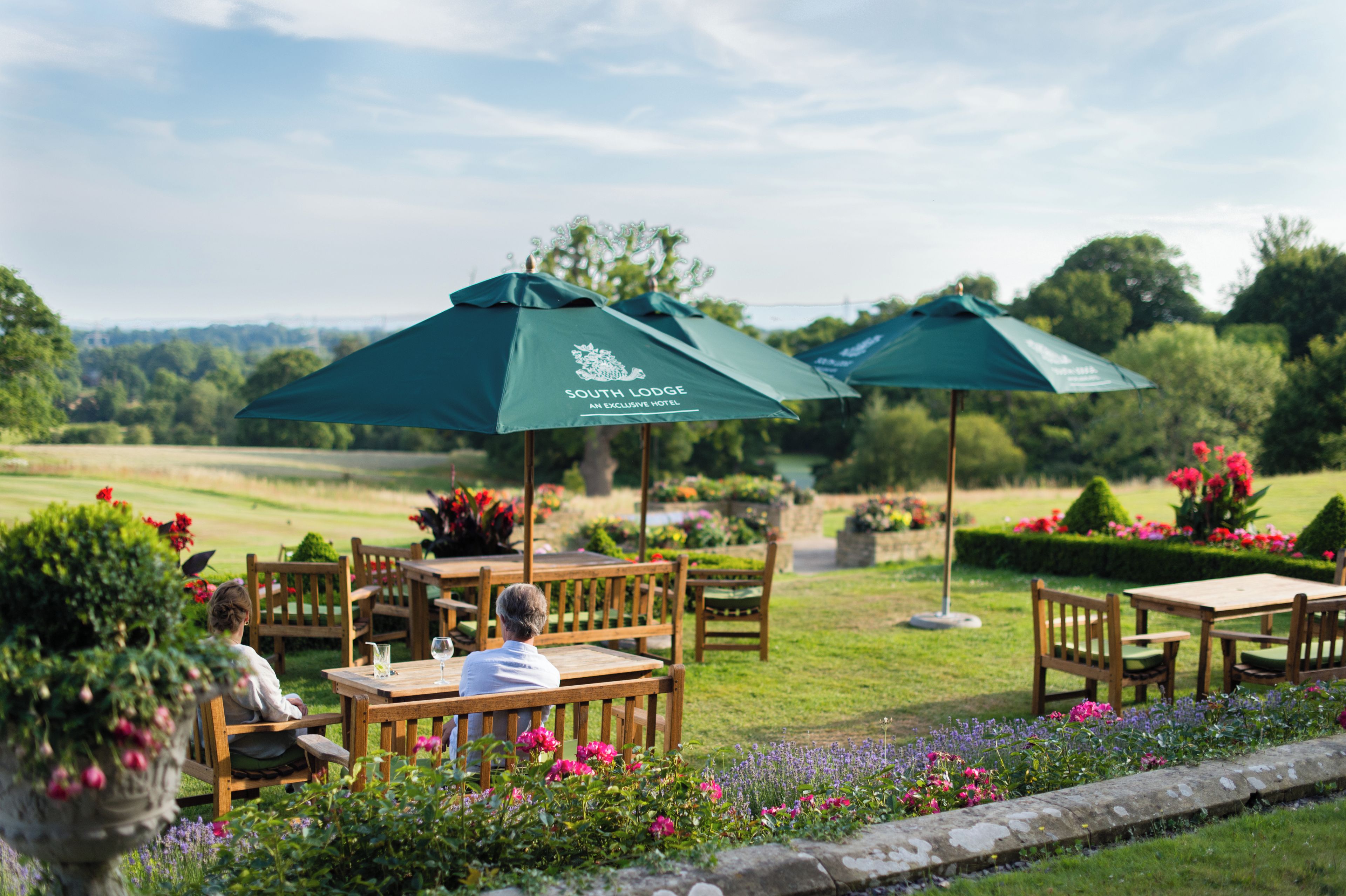 A South Lodge outdoor seating area with tables and chairs, surrounded by flower beds and greenery.