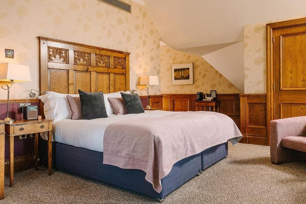 A bedroom with a large bed, wooden headboard, bedside tables, and a patterned carpet.