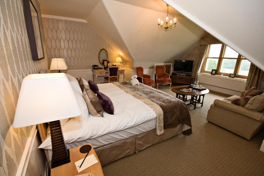 A hotel room with a large bed, a sitting area with a table, a TV, and a window.