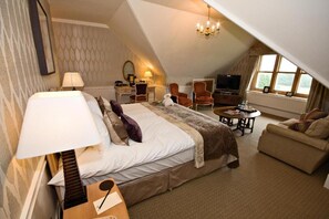 A hotel room with a large bed, a sitting area with a table, a TV, and a window. - South Lodge (Sussex)