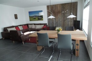 A modern living room with a wooden dining table, two chairs, a sofa, and a TV. - Holiday apartment with 2 bedrooms (Mittenwald)