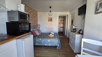 A compact hotel room with a kitchenette, a bed with floral bedding, a small desk, and a television.