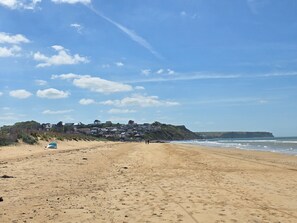 A sandy beach with a clear sky, a few scattered clouds, and a distant view of houses on a hill. - Studio 'Charmant Bord De Mer' with Private Terrace, Shared Garden and Wi-Fi (Saint-Côme-de-Fresné)