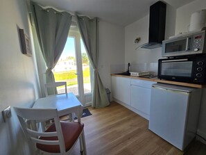 A compact kitchen with a microwave, toaster, and sink. There is a dining table with a chair. - Studio 'Charmant Bord De Mer' with Private Terrace, Shared Garden and Wi-Fi (Saint-Côme-de-Fresné)