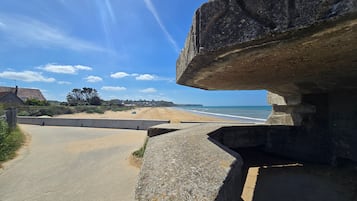 Een kustweg met een stenen brug, die leidt naar een strand met huizen op de achtergrond.