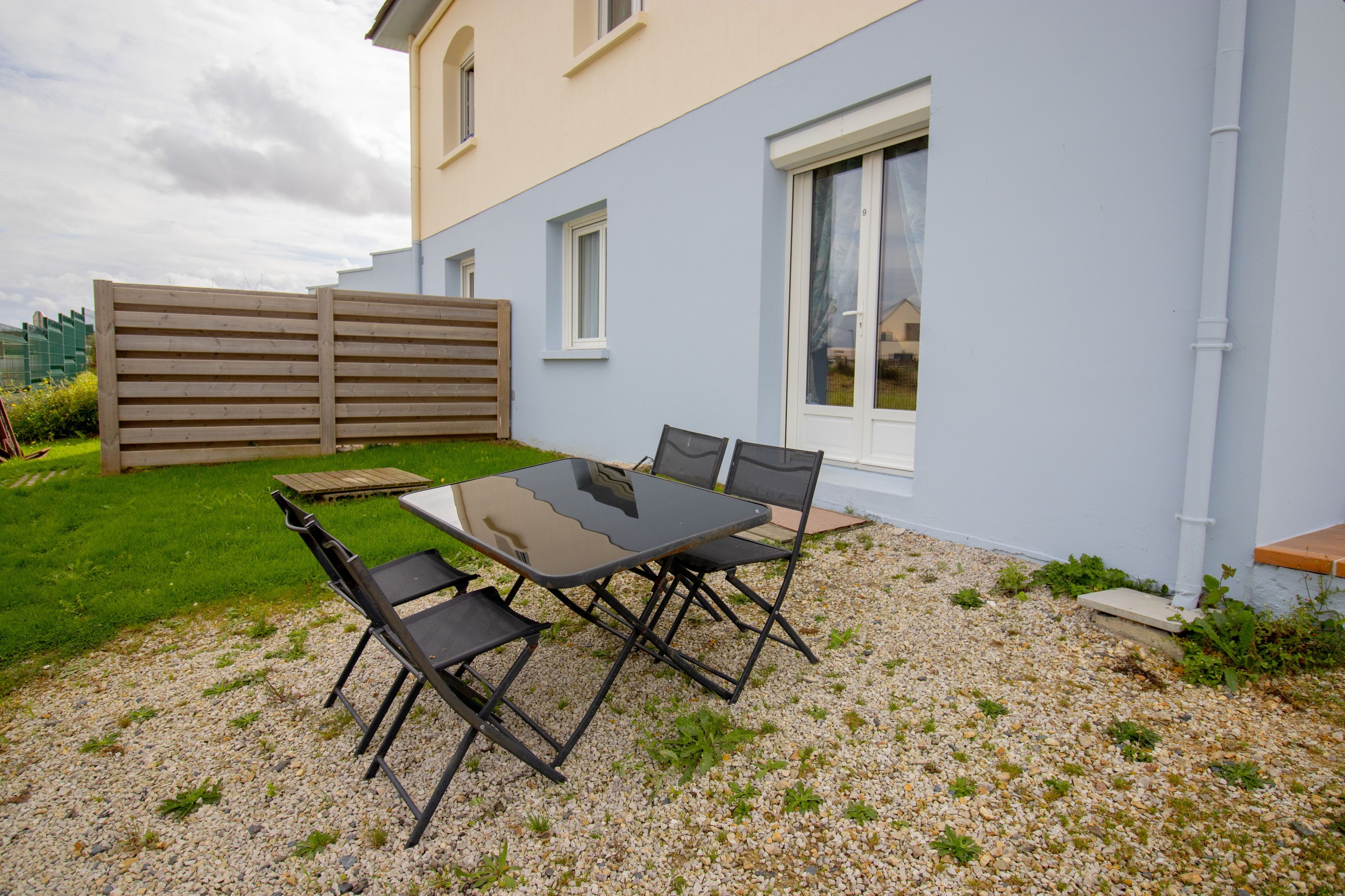 Eine Terrasse mit Tisch und Stühlen, ein Holzzaun und ein Gebäude mit Fenstern.