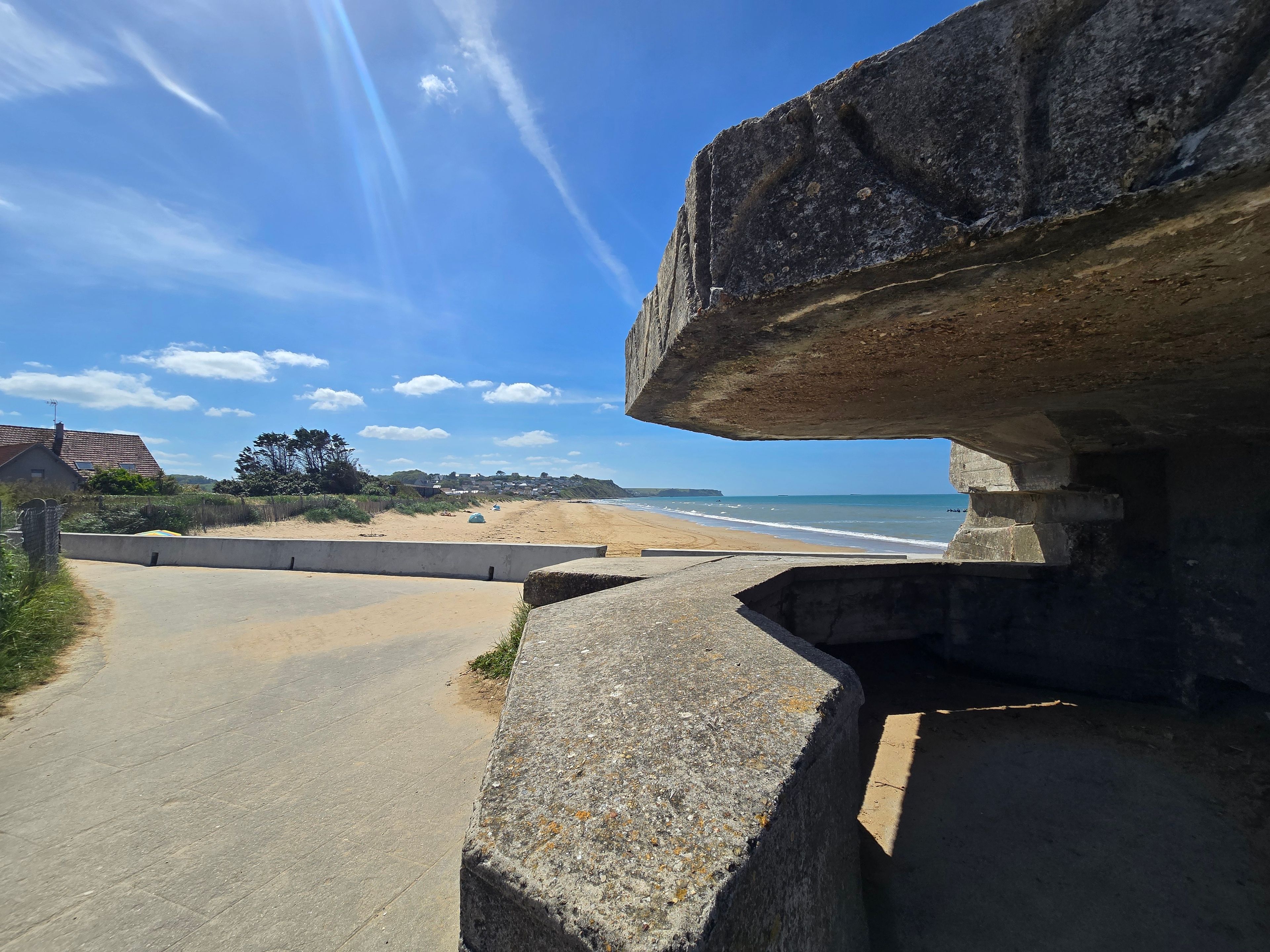 A coastal road with a stone bridge, leading to a beach with houses in the background.