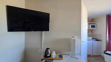 A room with a flat-screen TV mounted on the wall, a small kitchenette with a microwave, and a table with a kettle and a tray of items.