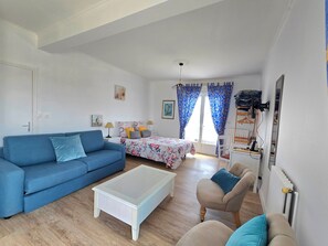 Ein Zimmer mit einem blauen Sofa, einem weißen Couchtisch, einem Bett mit floralem Bettbezug und einem Sessel mit Kissen.