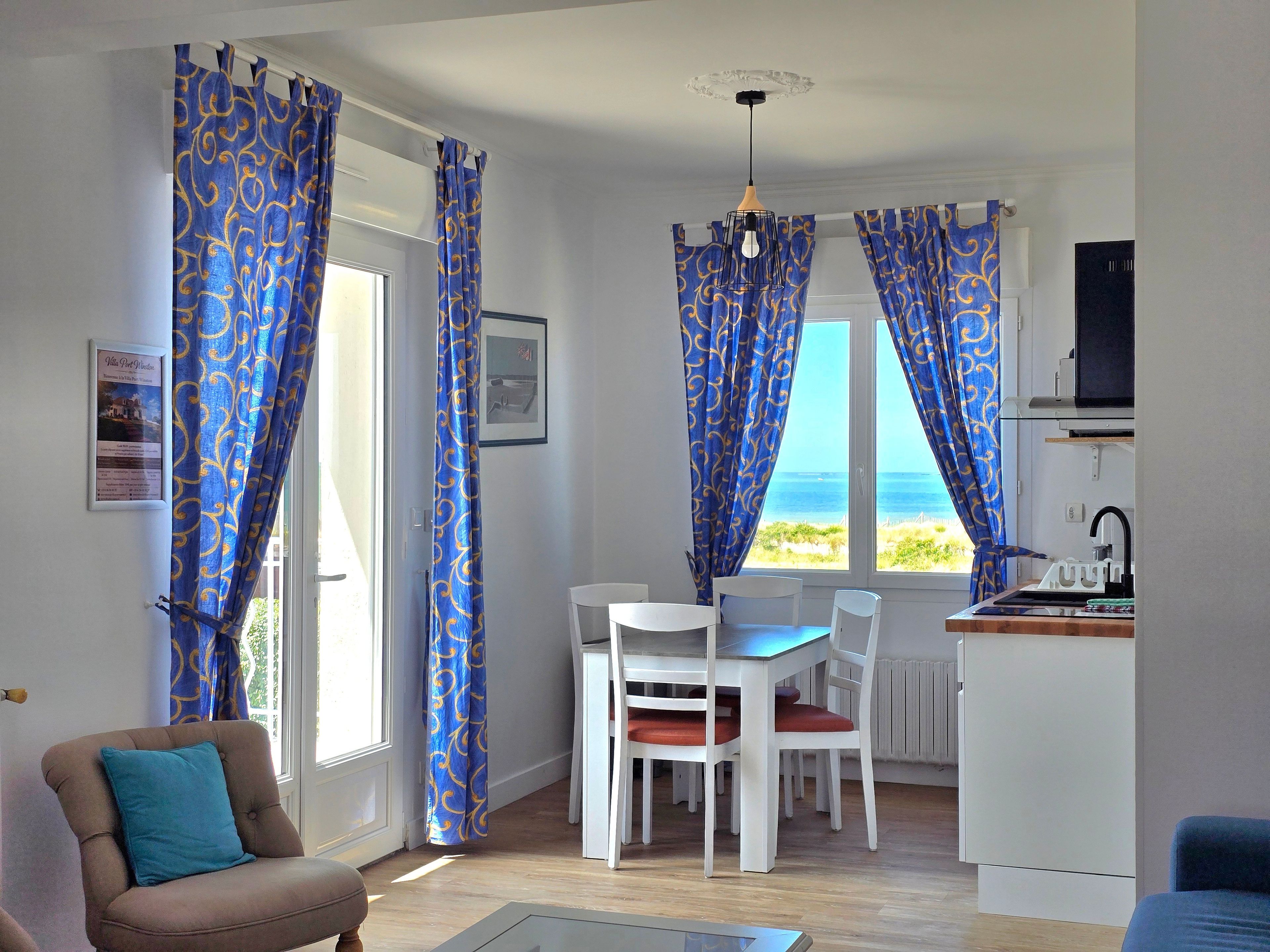 Une pièce comprenant une table à manger et des chaises, avec vue sur la mer, et un coin cuisine.