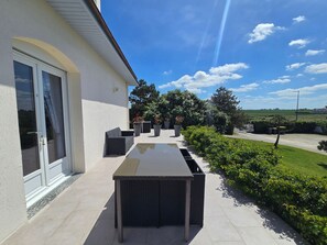 Eine Terrasse mit Tisch und Stühlen, eine Glastür und Blick auf eine grüne Landschaft.