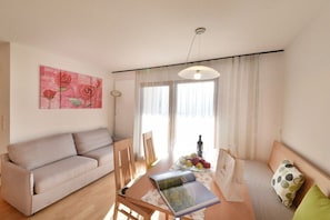 A living room with a sofa, a dining table with chairs, a book, and a vase with flowers. - House Rosengarten C&D (Dorf Tirol)