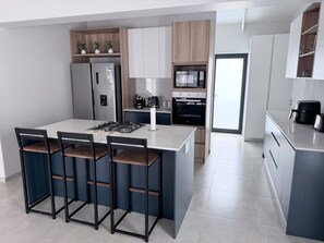 A modern kitchen with a central island, bar stools, built-in appliances, and a view to the dining area. - Home from home with an indoor braai, 700 m to the Golden Mile (Saint Helena Bay)