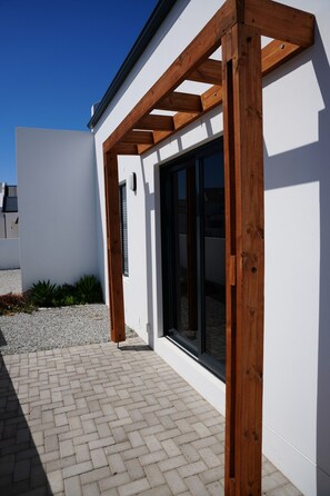 Een modern gebouw met een witte gevel, een houten pergola en een betegeld terras.