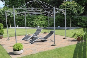 Ein Kiosk mit Metallgestell, zwei Lounge-Stühlen und einem Blumentopf.