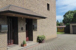 Ein Backsteinhaus mit überdachter Veranda, einem kleinen Garten und einem gepflasterten Zugang.