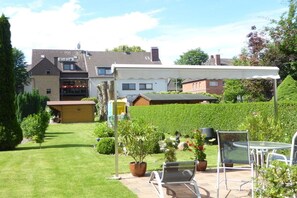 Ein Wohnhaus mit gepflegtem Rasen, einer Sitzgelegenheit im Freien und einer überdachten Terrasse.