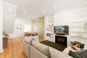 Een moderne woonkamer met een bank, een open haard en een eethoek op de achtergrond.