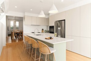 Een moderne keuken met een centraal eiland, barkrukken, roestvrijstalen apparatuur en een eethoek met een tafel en stoelen.