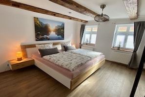 A bedroom with a large bed, wooden beams, a painting, and a window with curtains. - Mountain apart 5||Wernigerode (Wernigerode)