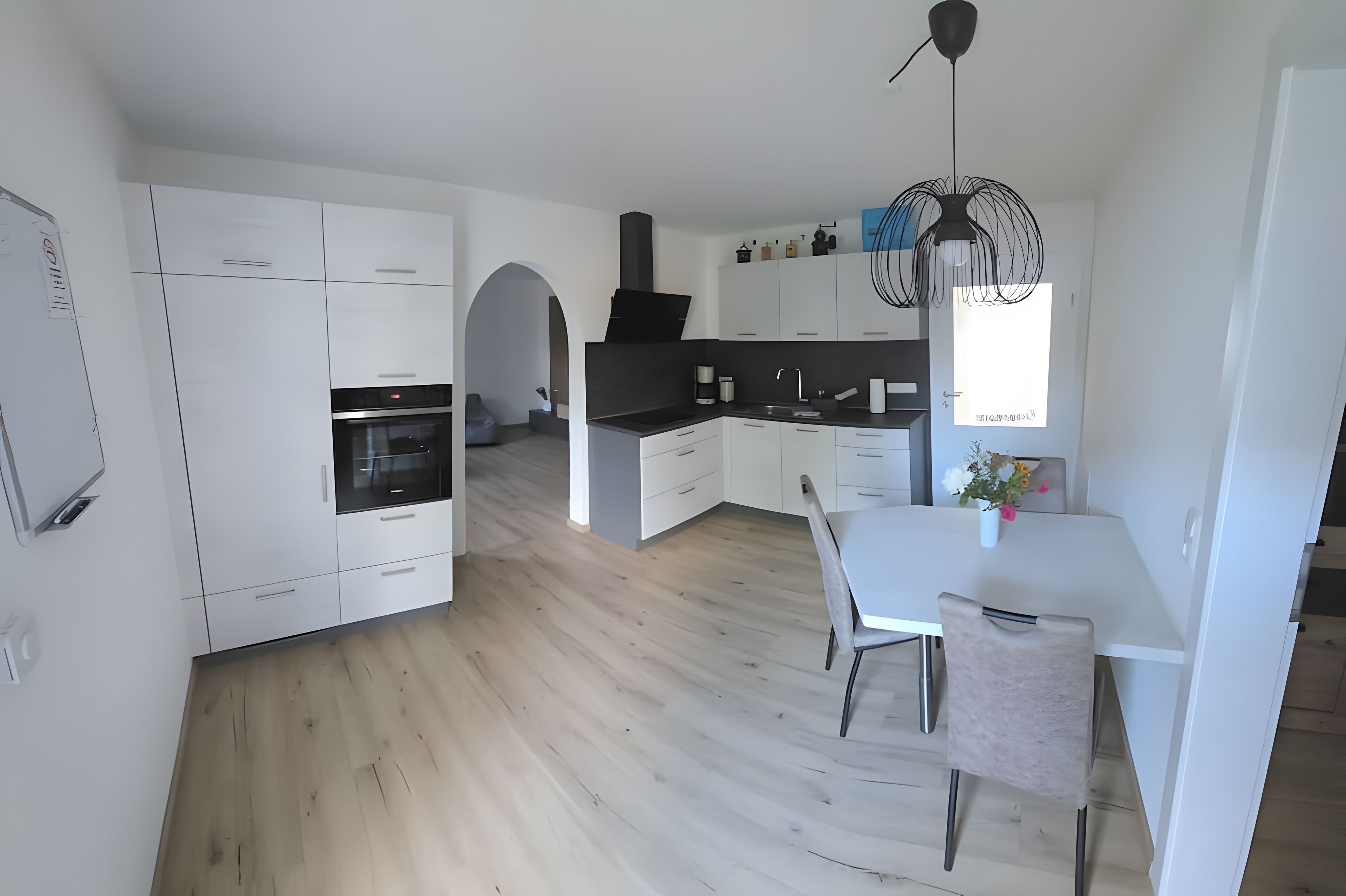 Una cocina moderna con armarios blancos, una isla central y un comedor con mesa y sillas.