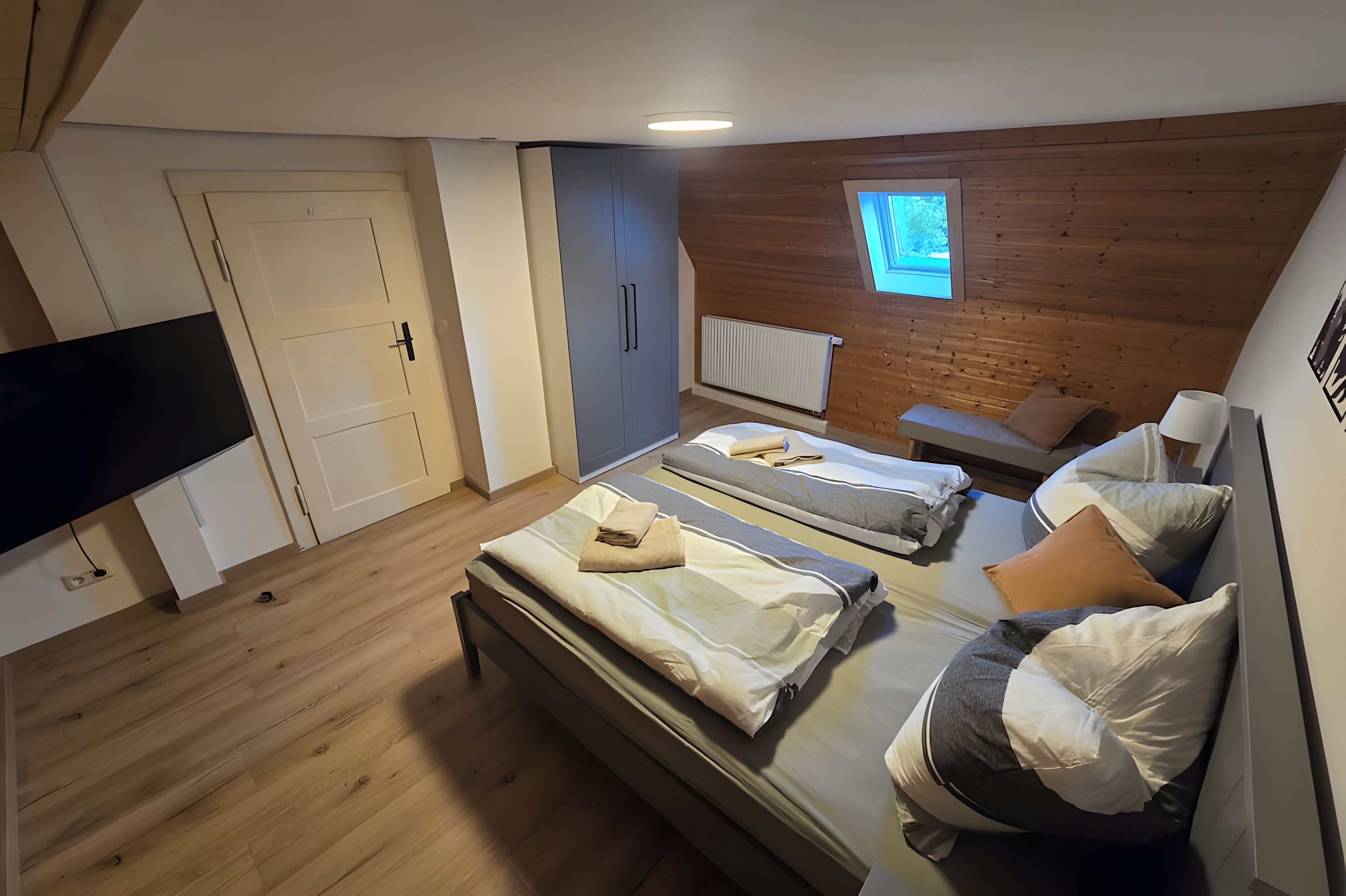 Un dormitorio con dos camas, televisión, ventana y techo de madera.