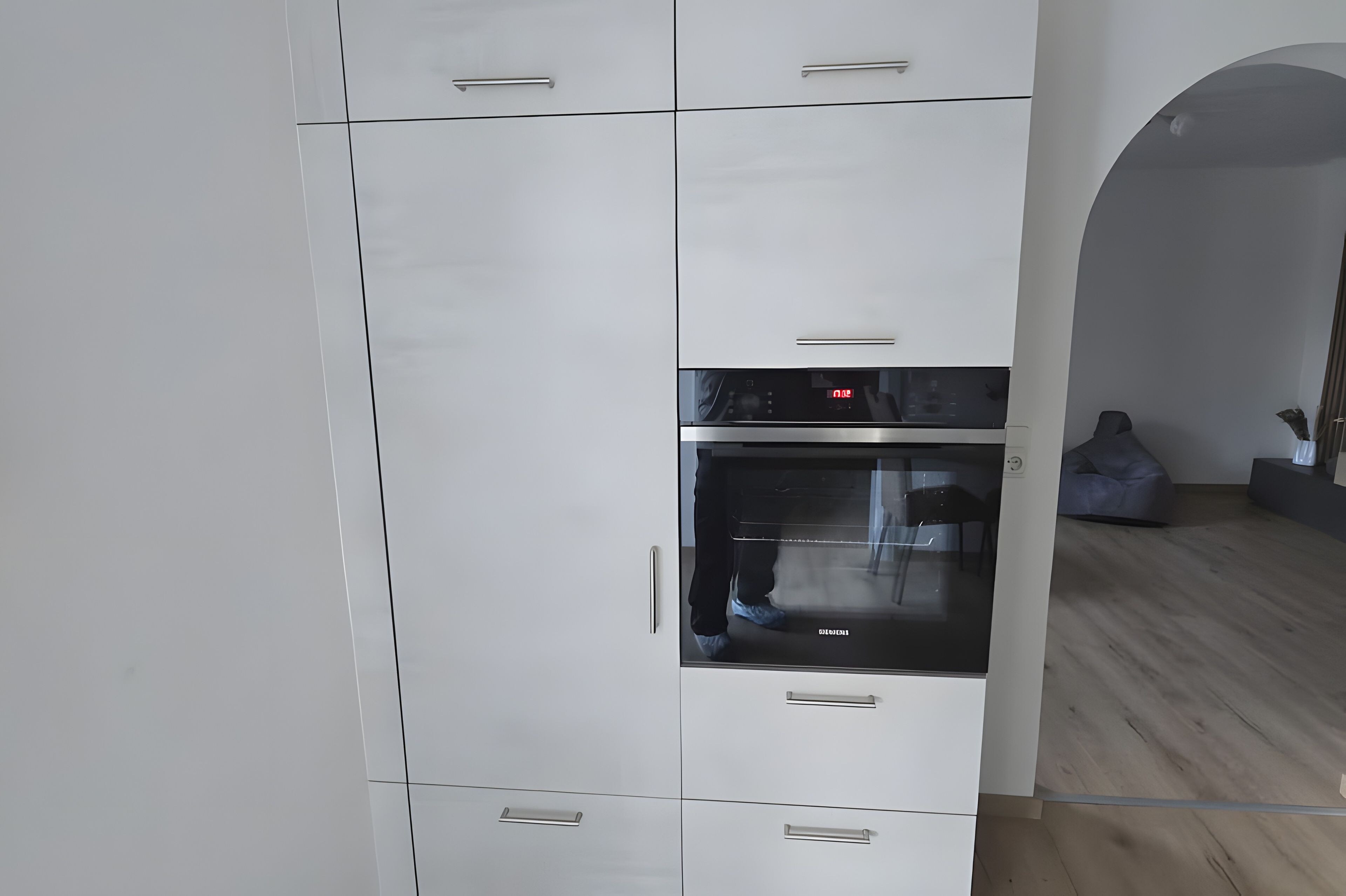 Een moderne keuken met witte kastjes, een ingebouwde oven en een koelkast met glazen deur.