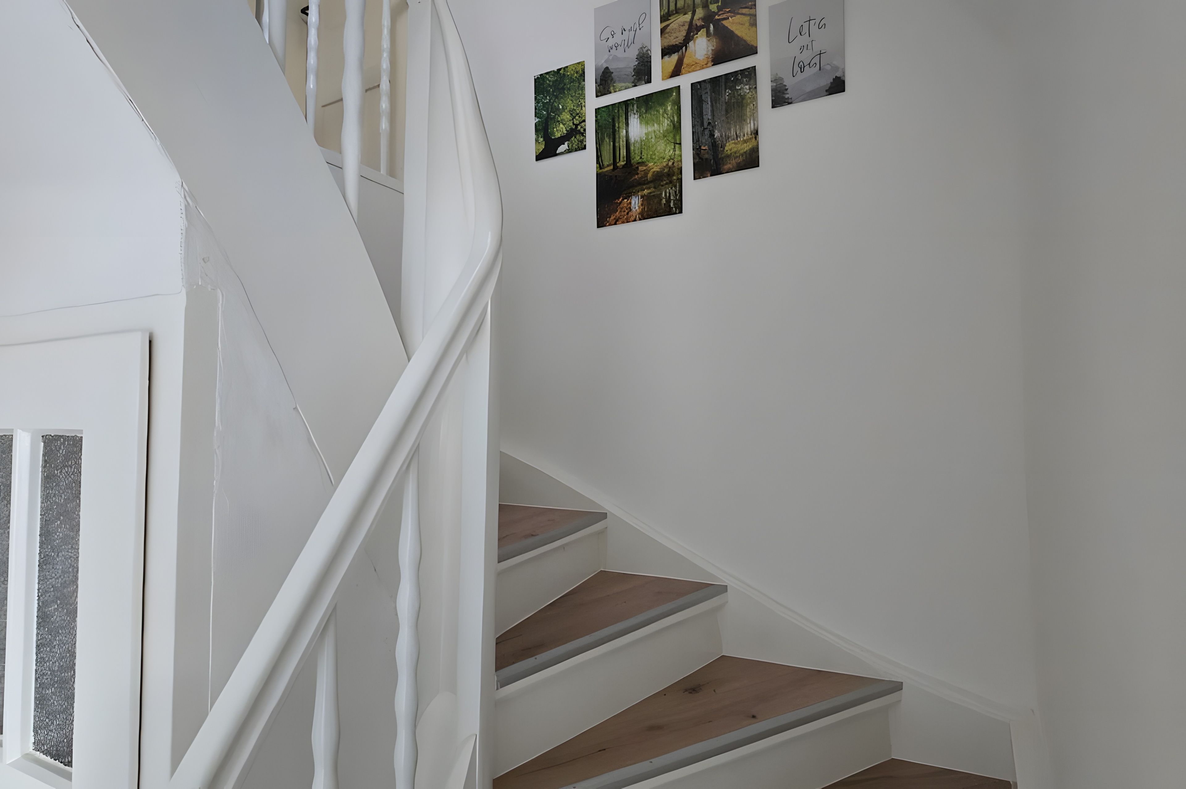 Eine Treppe mit weißen Geländern und Holzstufen, die zu einer Empfangsebene führt, auf der Bilder an der Wand hängen.