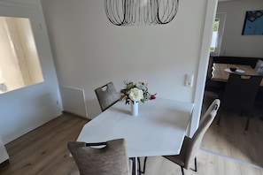 Ein Essbereich mit einem weißen Tisch, grauen Stühlen und einer Vase mit Blumen.